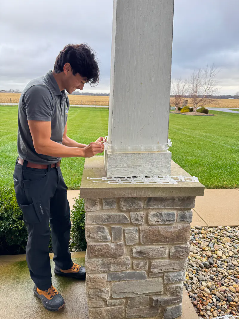Wrapping a porch column with a light strand, measuring the spacing by hand