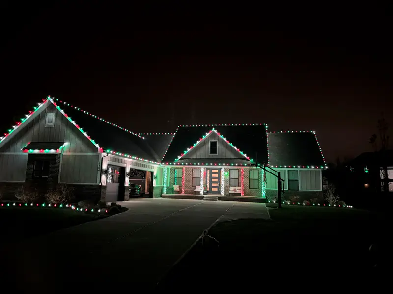 Craftsman house with red, green and white bulbs on every gable and a lit driveway edge