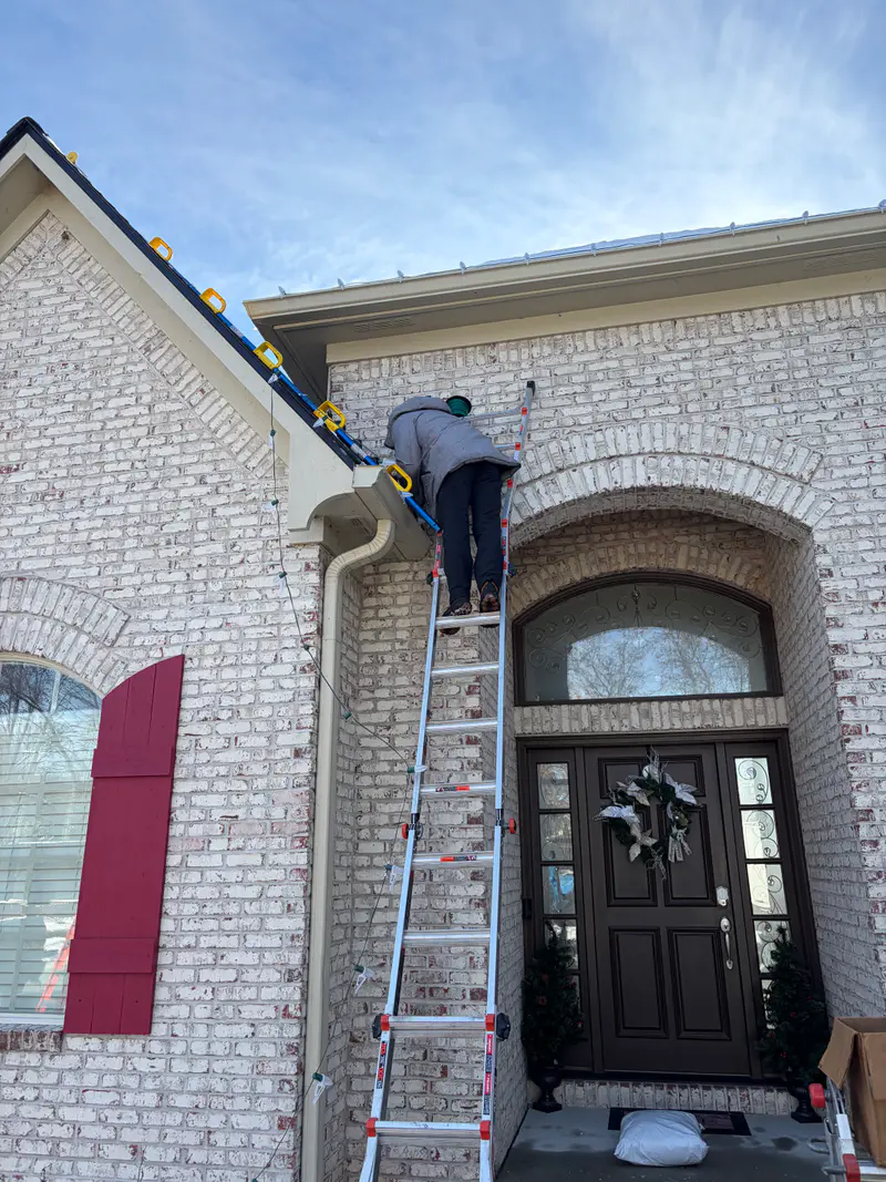 Installer on a ladder above an arched front door with red shutters, running the top line