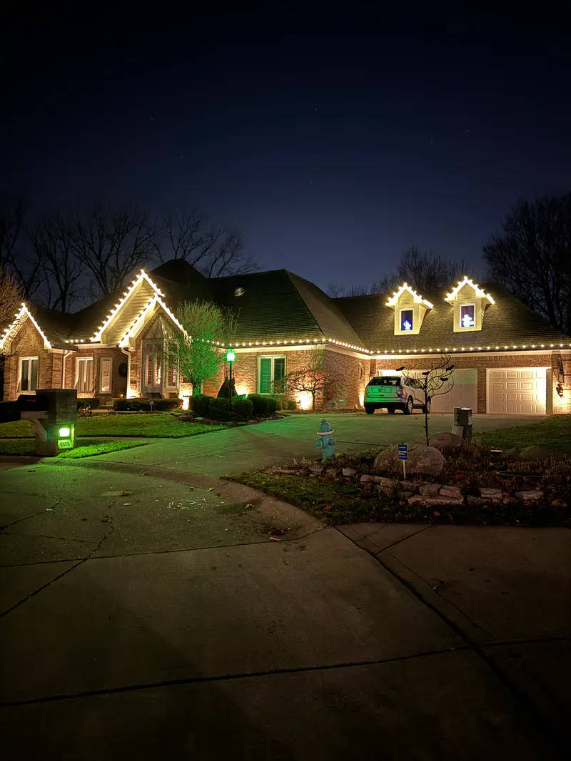 Brick house with twin dormers and a wide gable outlined in warm white bulbs above a curved front walk