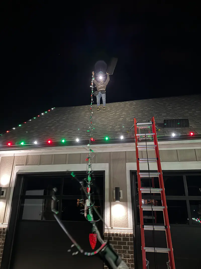 Ladder up to a garage roof at night while the red, green and white eave line is finished