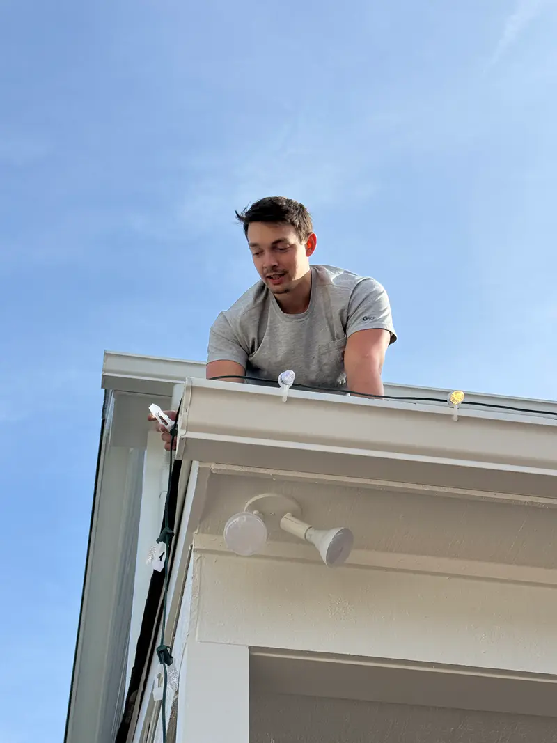 Installer leaning over a gutter line from a ladder, fitting clips along the eave