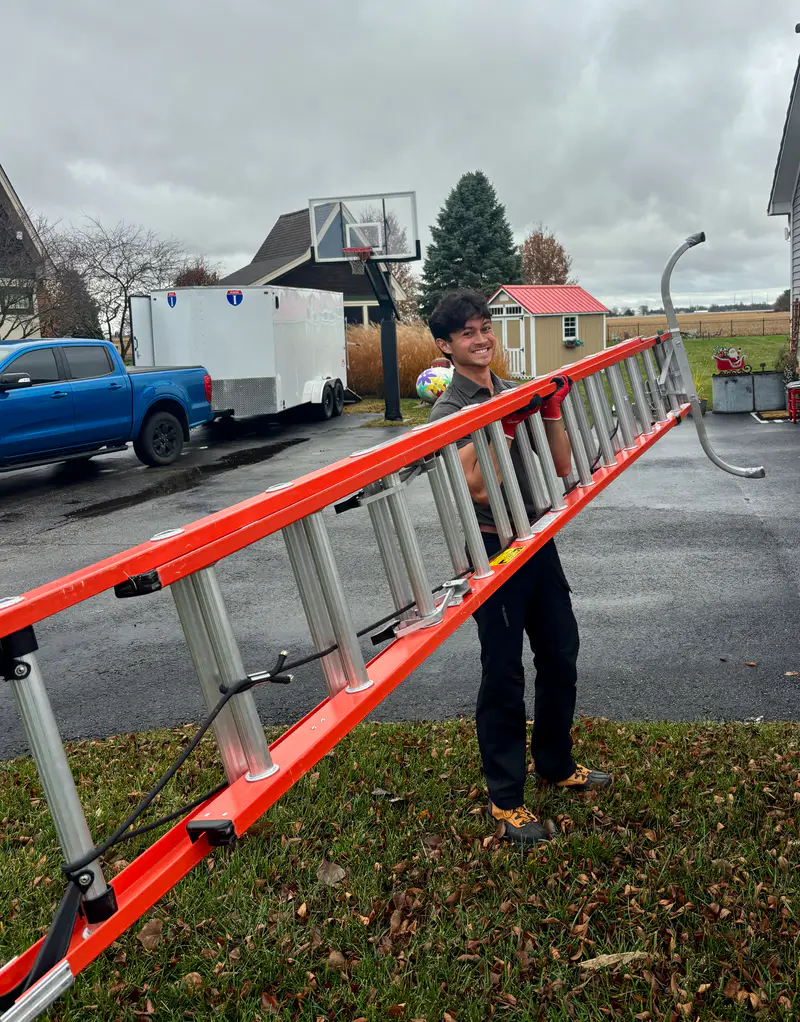 Carrying an extension ladder across the lawn on install day, truck and trailer behind