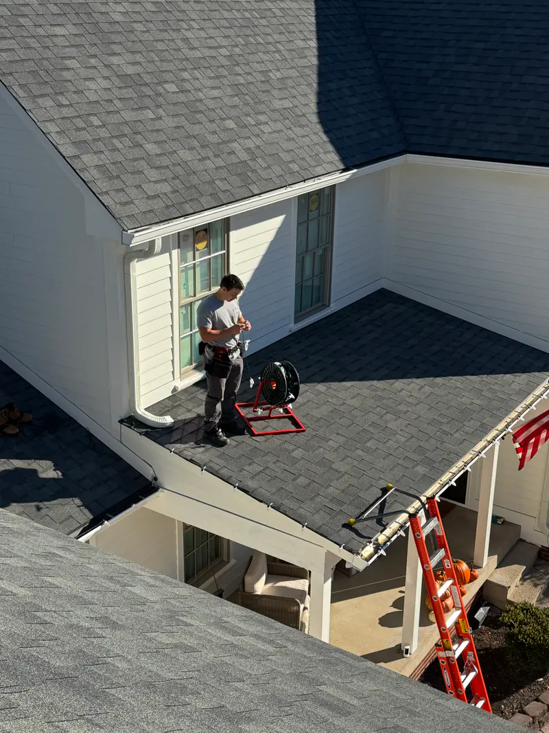 Installer on a lower roof with a reel of wire, seen from the roof above