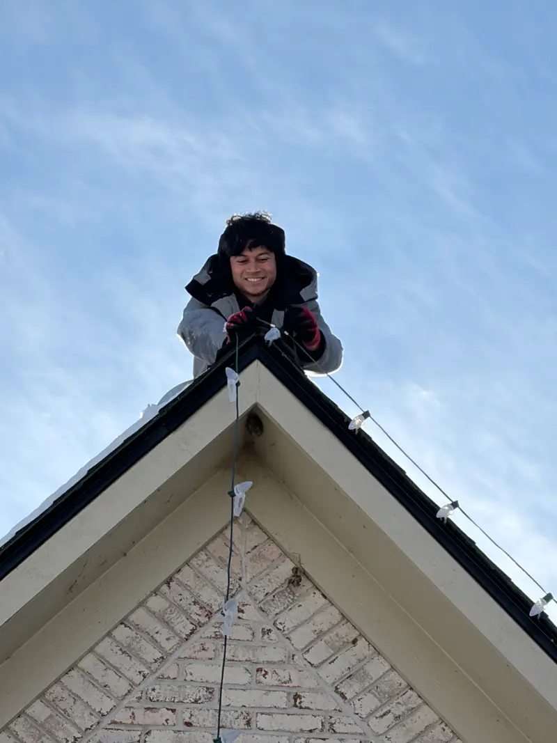 Kyle at the very peak of a brick gable, clipping the top bulb in place