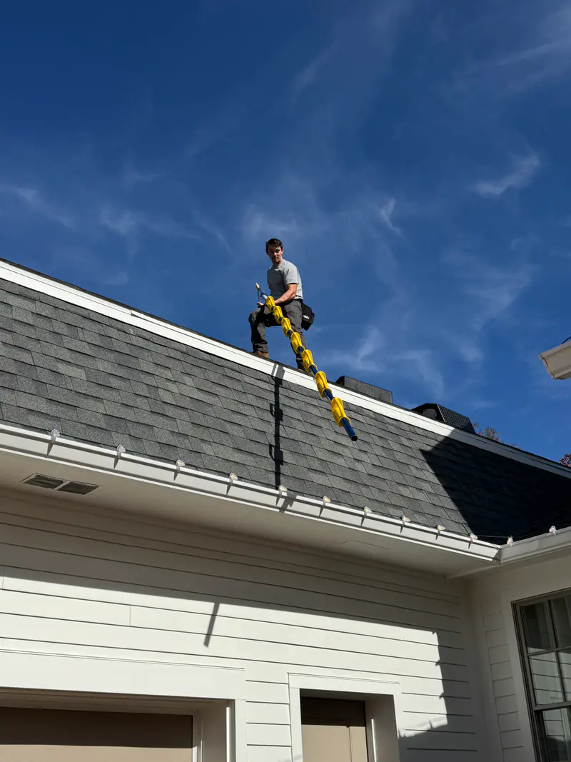 Installer walking a roof under a clear blue sky with a strand of bulbs