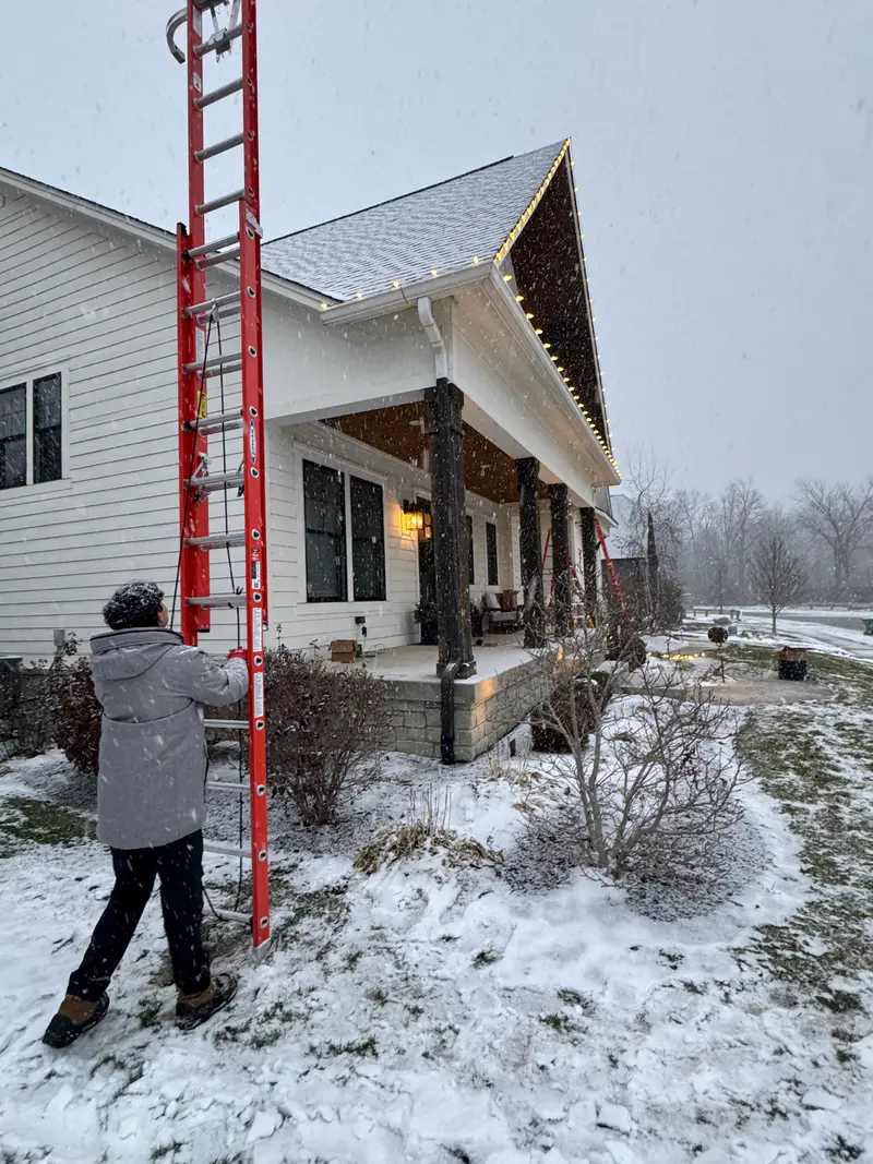 Ladder against a gable in the snow while an installer works the lights mid season