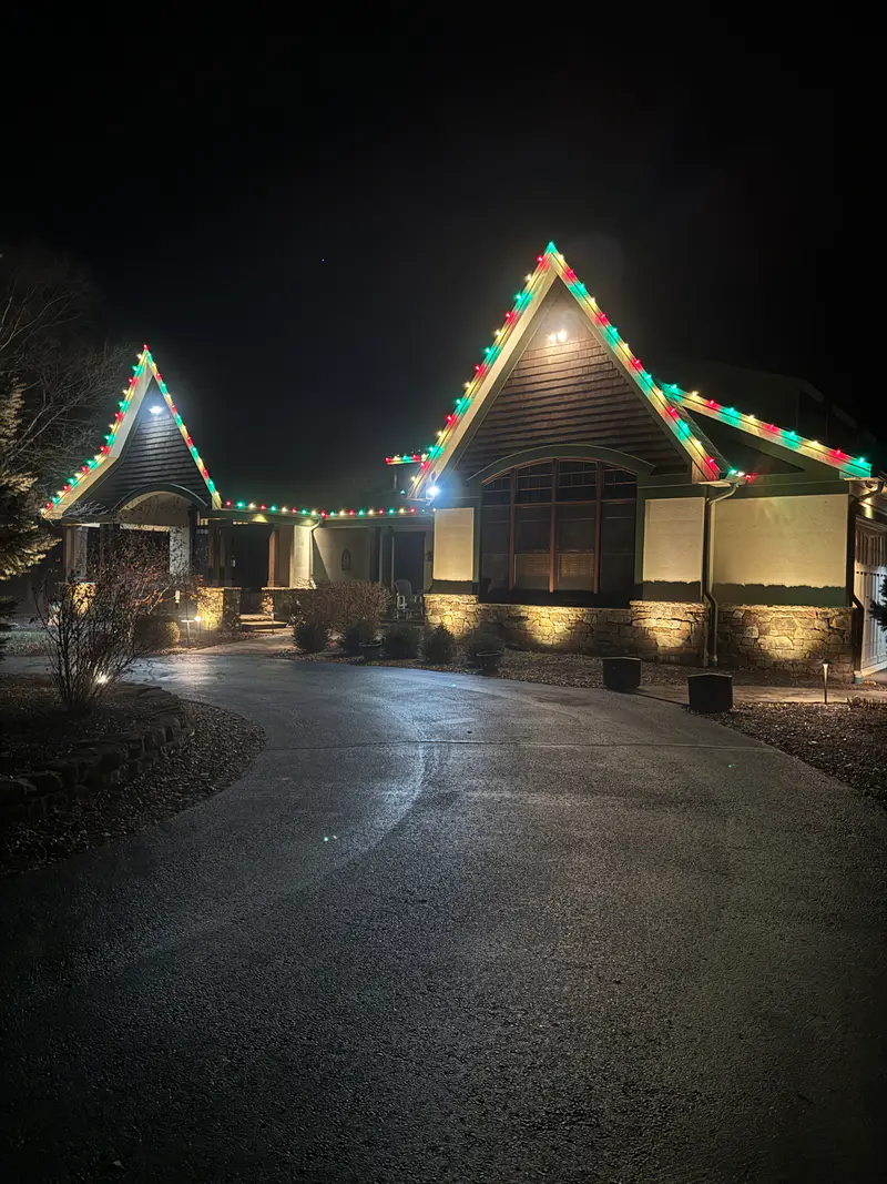 Two steep gables outlined in red, green and white bulbs above a wet curving driveway