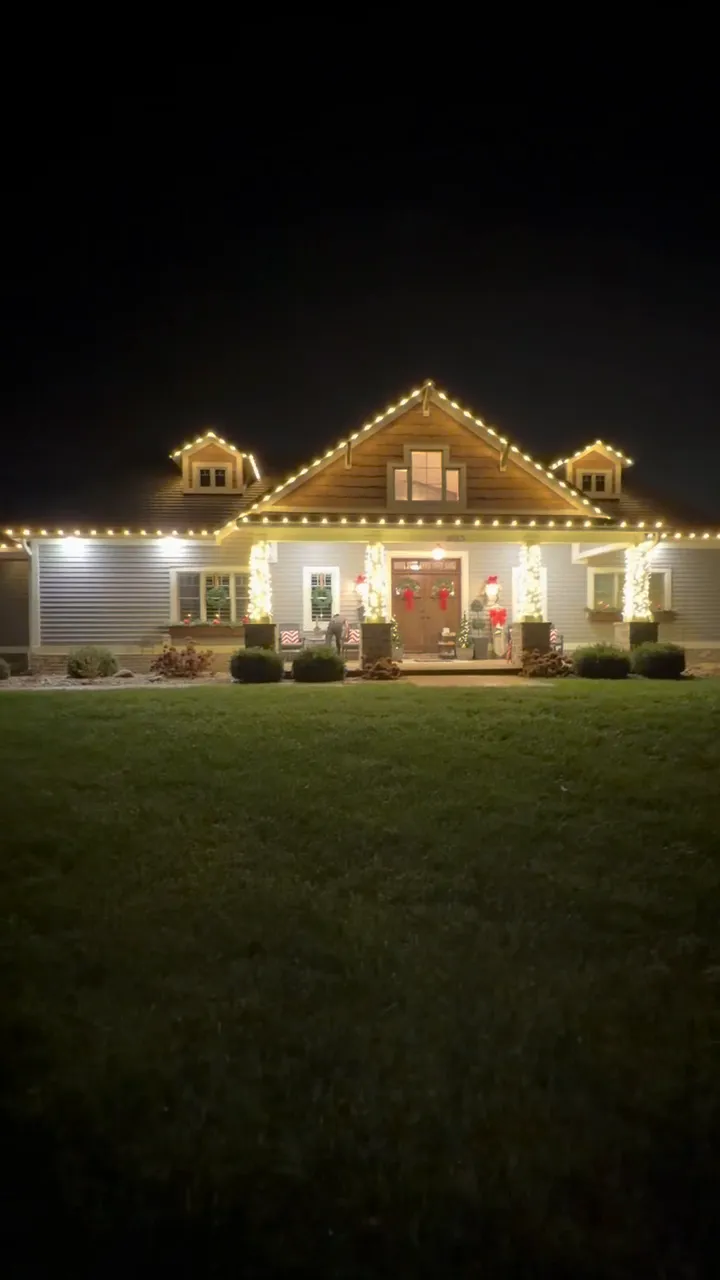 The same house a second later with every roofline, dormer and column lit in warm white
