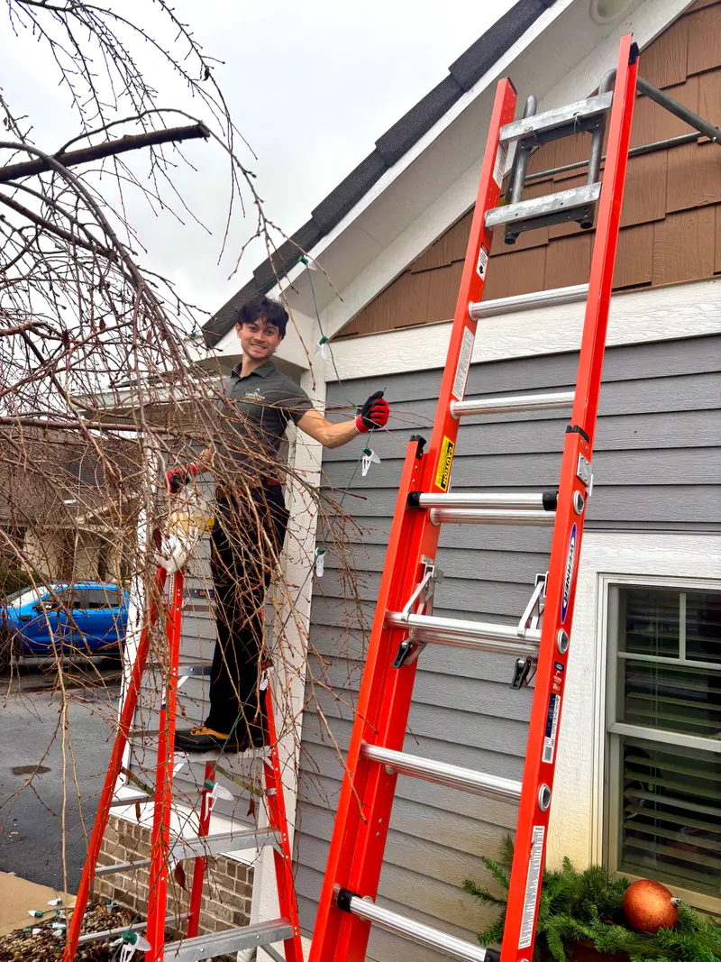 Two ladders against a gray sided house while an installer works the gable